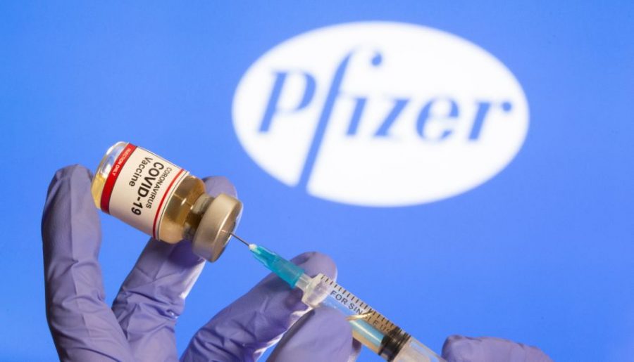 A woman holds a small bottle labeled with a Coronavirus COVID-19 Vaccine sticker and a medical syringe in front of displayed Pfizer logo in this illustration taken, October 30, 2020. REUTERS/Dado Ruvic - RC29TJ9CENFB